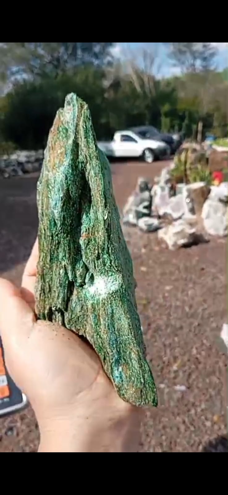 Pedra de coleção verde intensa segurada à mão, mostrando textura e veios naturais